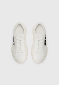 Sneakers bianche con lacci, dalla texture liscia, punta rotonda e logo nero "DKNY" sul lato. Presentano una suola rigata per una migliore presa.