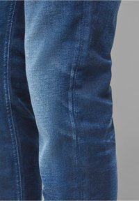 Jeans i denim i djupblått med en subtil blekning. Tyget har en mjuk struktur med synliga sömmar längs skarven och konturerna.