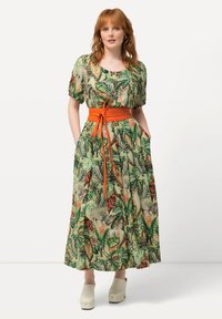 Maxikleid aus grünem Stoff mit einem Dschungeltier-Muster. Kurze Puffärmel, taillierter oranger Gürtel und seitliche Taschen.