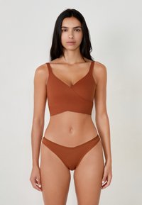 Bralette marrone senza cuciture con un design incrociato e spalline larghe, abbinata a slip bikini marroni coordinati. Texture liscia.