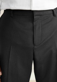 Black dress trousers made from a smooth material, featuring a flat front, waistband with belt loops, and subtle crease lines down the legs.