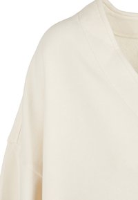 Crème kleurige pullover sweatshirt met een v-hals, textuurstof en verlaagde schoudernaden. Heeft een ontspannen pasvorm en gestikte details.