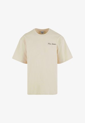 Tejszínes pamut póló, laza fazonnal. Rövid ujjú és kerek nyakú. A "Kani Studios" felirat sötétbarna színnel van nyomtatva a bal mellrészen.