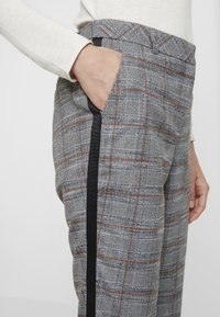 Pantalons gris à carreaux avec des bandes latérales noires ; présentent un tissu texturé et des poches sur le devant, montrés sur le côté d'un modèle.