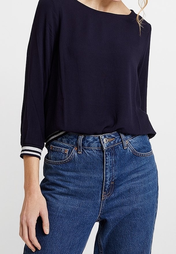 Top blu navy ampio con maniche a tre quarti e polsini a righe bianche, abbinato a jeans in denim blu a vita alta.