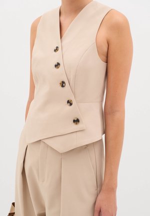 Beige ärmelloses Oberteil mit V-Ausschnitt, asymmetrischem Saum und fünf Schildpattknöpfen vorne, aus glattem Stoff gefertigt.