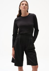 Czarny top z długim rękawem w połączeniu z czarnymi szortami o wysokim stanie, plisowanymi, wykonanymi z gładkiego materiału, charakteryzującymi się luźnym krojem i minimalistycznym designem.