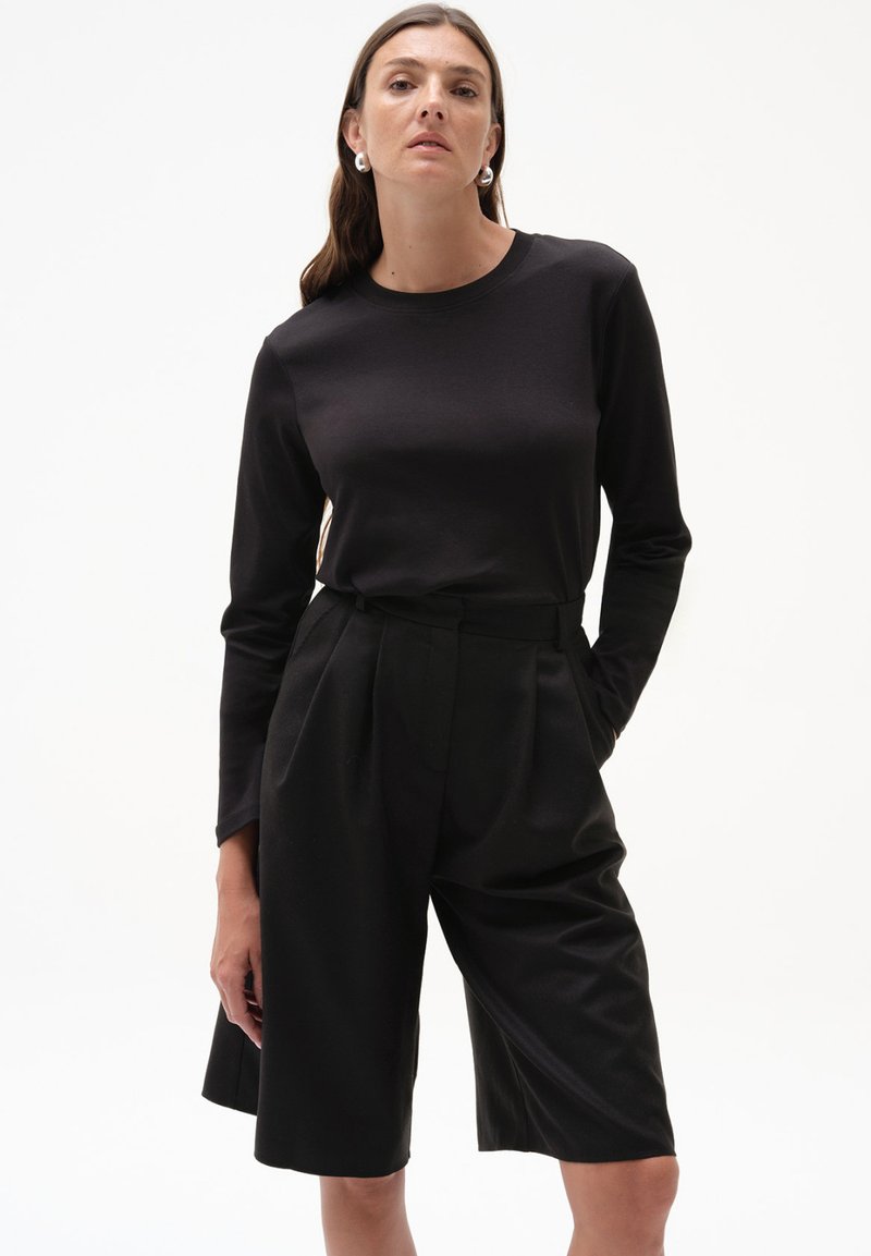 Czarny top z długim rękawem w połączeniu z czarnymi szortami o wysokim stanie, plisowanymi, wykonanymi z gładkiego materiału, charakteryzującymi się luźnym krojem i minimalistycznym designem.