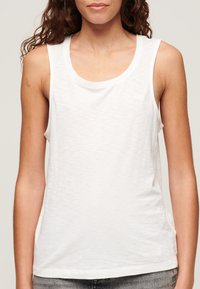 Witte katoenen tanktop met een ronde halslijn, mouwloos ontwerp en een subtiele textuur. Bevat een klein logo op de borst.