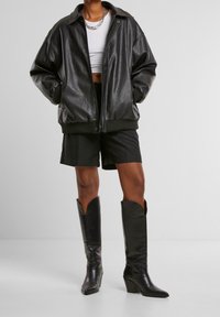 Černá kožená bomber bunda s oversize střihem, žebrovanými manžetami a zipovým uzávěrem. V kombinaci s černými šortkami a kozačkami na podpatku ke kolenům.