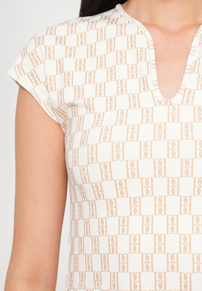 Topp med kort ärm i vitt tyg med ett upprepande ljusorange geometriskt mönster; har en v-ringning och mjuk textur.