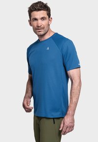 Kurzärmliges blaues Sportshirt aus strukturiertem Stoff mit Rundhalsausschnitt und Logo auf der Brust, kombiniert mit olivgrünen Hosen.