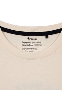 Camiseta de color beige claro con escote redondo y ribete negro. La etiqueta interior incluye mensajes sobre reciclaje e instrucciones de cuidado. Etiqueta de tamaño "M".