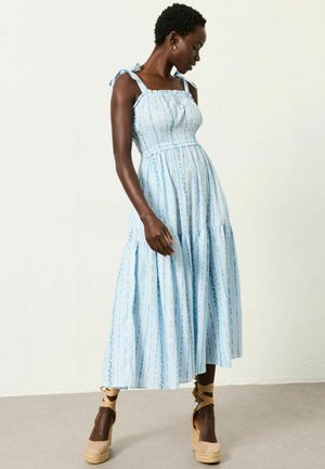 Hellblaues Kleid mit Blumen- und Streifenmustern, gerafftem Oberteil, verstellbaren Trägern zum Binden und mehrlagigem Rock. Kombiniert mit Keilsandalen aus Espadrille.