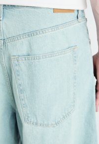 Shorturi din denim de culoare albastru deschis, cu un buzunar pe spate și detalii de cusătură minime. Materialul are o textură moale și un design casual.