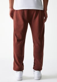 Pantaloni da tuta bordeaux con una vestibilità comoda, texture morbida e gambe affusolate. Indossati con sneakers bianche, caratterizzate da un design semplice e privo di decorazioni.