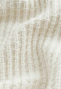 Texturiertes cremefarbenes Strickgewebe mit einem Gittermuster, das eine weiche, flauschige Oberfläche erzeugt. Ideal für warme Bekleidung oder Decken.