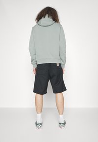 Grön huvtröja med avslappnad passform och framficka, tillsammans med svarta shorts. Har gröna rutiga skor och vita strumpor.