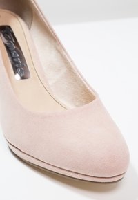 Gros plan sur une chaussure pour femme en daim rose clair, avec un bout arrondi et une doublure intérieure beige rembourrée.