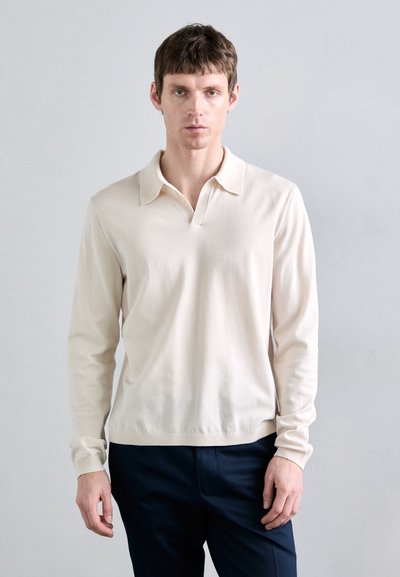 Beige Langarm-Polo mit Kragen und halben Knopfverschluss. Hergestellt aus weichem Material mit gerippten Bündchen. Mit einer taillierten Silhouette designt.
