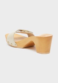 Wedge heeled sandal in off-white leather with a smooth texture and decorative brass studs, featuring a natural wood-like heel.