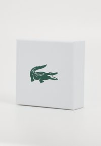 Hvit boks med en teksturert overflate, med en grønn krokodille-logo på fronten, som viser en minimalistisk design.