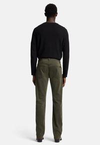 Maglione scuro e pantaloni verde oliva con taglio dritto. I pantaloni hanno due tasche posteriori, cuciture visibili e una trama sottile.