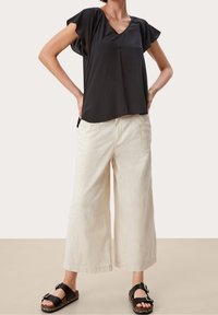 Blusa nera a maniche corte con scollo a V, abbinata a pantaloni larghi color crema e sandali neri con dettaglio della fibbia.