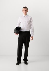 Weißes Hemd mit Kragen, schwarzer Gürtel, lockere schwarze Hose und schwarze Lederhandtasche. Glatter Stoff und taillierte Passform.