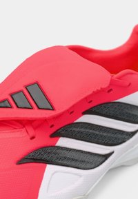 Φωτεινό ροζ αθλητικό παπούτσι με υφή στην επάνω επιφάνεια, μαύρες λεπτομέρειες και τρεις άσπρες ρίγες. Διαθέτει επενδεδυμένη γλώσσα και σύστημα κορδονιών.