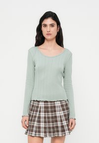 Ανοιχτό πράσινο μακρυμάνικο ριμπ τοπ με στρογγυλή λαιμόκοψη, συνδυασμένο με πλισέ καρό φούστα σε καφέ και λευκό χρώμα, με ανομοιόμορφο τελείωμα.