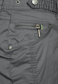 Shorts cargo en tissu gris avec une poche zippée, des détails boutonnés et des coutures contrastantes vertes. La texture semble lisse avec un design épuré.