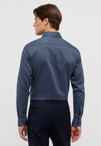 Camicia a maniche lunghe blu navy con motivo. Presenta piccoli disegni geometrici bianchi e un taglio dritto sull'orlo.