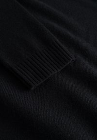 Schwarzer Strickpullover mit geripptem Ärmelbund, weicher Textur und glattem Finish, das das monochrome Design hervorhebt.