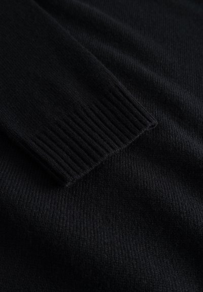 Suéter negro de punto con puños de manga acanalados, textura suave y acabado liso, que destaca su diseño monocromático.