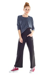 Graues Longsleeve-Shirt, schwarze weite Hose, pinke Sneakers. Das Shirt hat eine lockere Passform und dezentes Branding; die Hose verfügt über Seitentaschen.