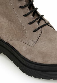 Gray suede ankle boot with black laces, featuring a textured upper and a chunky black rubber sole, detailed stitching along the seams.