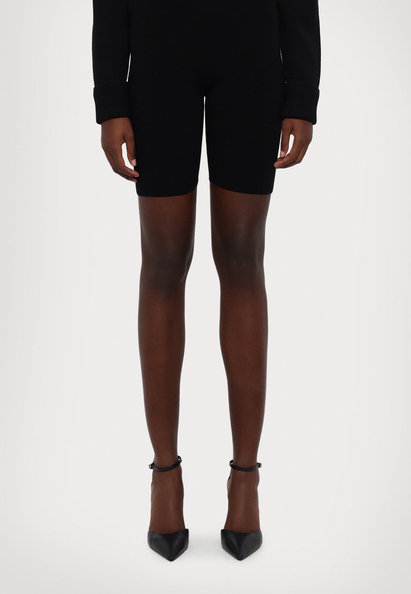 Body in maglia nera a maniche lunghe, abbinato a pantaloncini neri aderenti. Il modello indossa tacchi neri a punta con cinturini alla caviglia.
