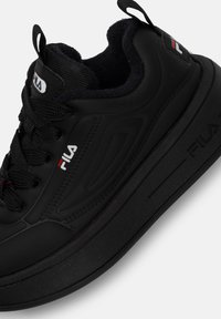 Czarne sneakersy Fila cechują się gładkim, skórzanym wykończeniem, teksturowanymi nakładkami, grubą gumową podeszwą oraz sznurowadłami, z akcentami logo na języku i boku.
