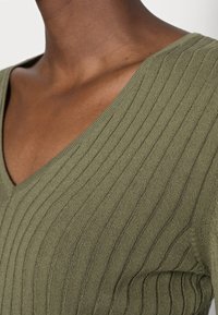 Olivgrön stickad topp med V-hals, med ribbad struktur och tight passform, som framhäver tygets stretch och mjukhet.