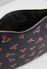Pochette zippée bleu marine avec un motif de cerises rouge et blanc. Extérieur texturé, doublure intérieure noire et fermeture éclair en métal doré.