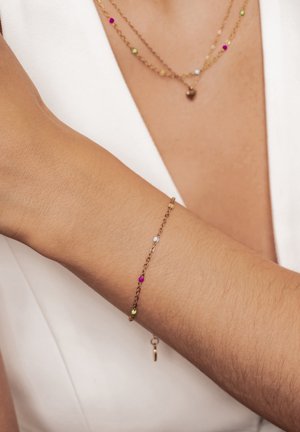 Delicate gold chain bracelet and layered necklace with small colorful beads worn on arm and neck over white fabric.