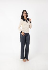 Cárdigan beige de canalé con cuello negro con volantes, puños negros y botones, combinado con pantalones de pierna ancha azul marino y zapatos transparentes.