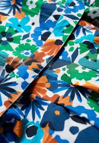 Țesătură cu imprimeu floral, oferind culori vibrante precum albastru, verde, portocaliu și negru. Textură netedă cu detalii în design pliat.