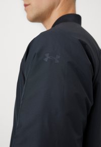 Giacca leggera nera realizzata in tessuto morbido, con un logo sottile sulla spalla e un design minimalista. Primo piano della manica.