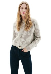 Pull gris clair avec un motif de feuilles subtil, col rond et poignets côtelés, associé à un jean taille haute bleu foncé et une ceinture blanche.