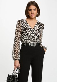 Blusa de estampado en blanco y negro con mangas transparentes, escote en V y cintura elástica, combinada con pantalones negros de tiro alto y un bolso.