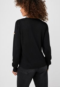 Maglione di lana nera con collo rotondo, maniche lunghe e orlo a coste. Presenta un delicato effetto a sbuffo sulle spalle e un accento ricamato sulla manica.