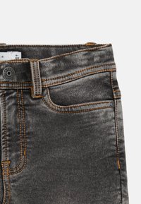 Gray denim jeans with orange stitching, featuring a button closure, front pockets, and a smooth, slightly worn texture.