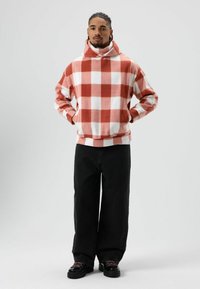 Rood-wit geruit fleece hoodie met een hoge kraag en losse pasvorm, gecombineerd met zwarte wijde broekspijpen en zwarte schoenen.